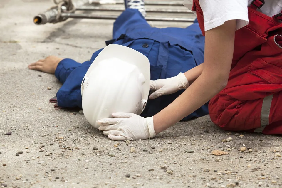 worker on the ground while another worker checks their pulse